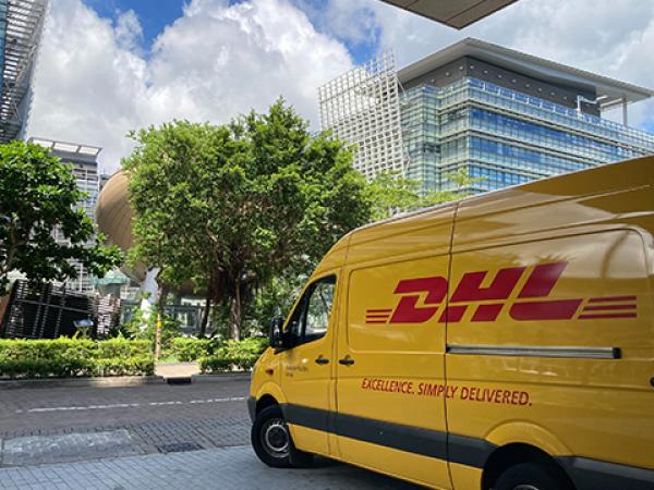 Gelber DHL-Lieferwagen vor Bürogebäude